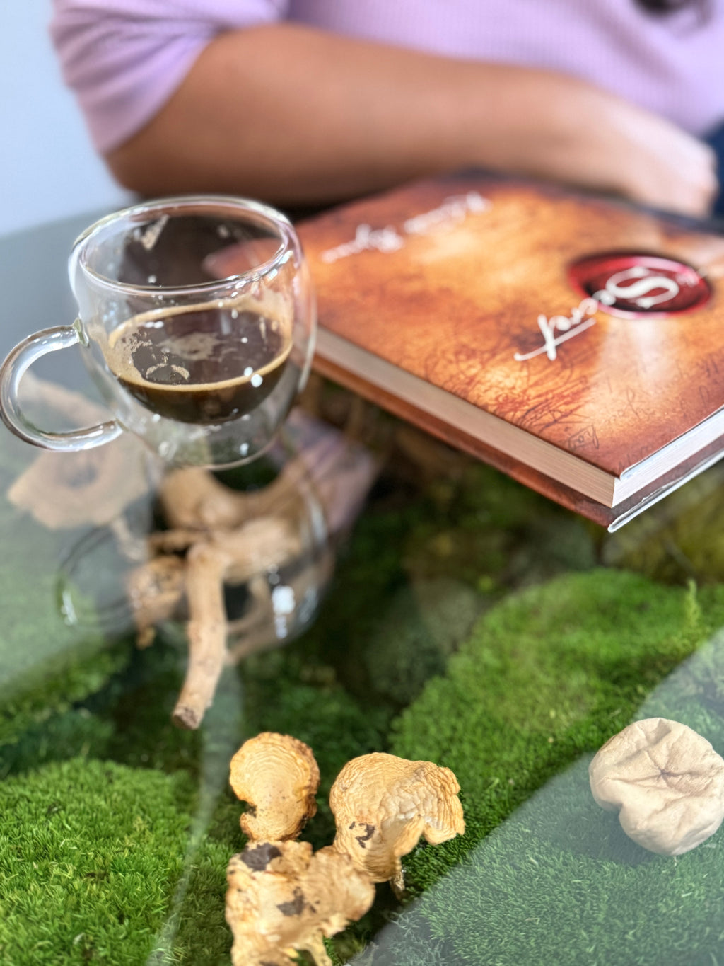Glass of coffee on a green surface with a book and small figurines.