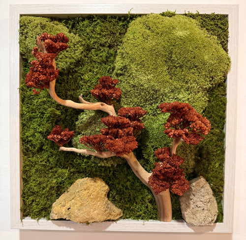 Framed artificial moss wall with red-brown branches and rocks on a white background